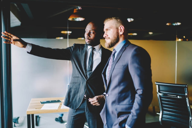 Invest Smart - 3 Little-Known Perks of Stock-Secured Loans That Could Change Everything; African american buisnessman pointing on smth standing near window with colleague talking about future plans, experienced male entrepreneurs discussing details for cooperation for project on meeting