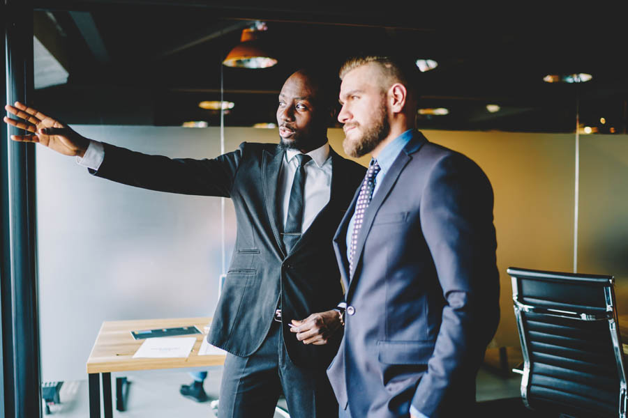 Invest Smart - 3 Little-Known Perks of Stock-Secured Loans That Could Change Everything; African american buisnessman pointing on smth standing near window with colleague talking about future plans, experienced male entrepreneurs discussing details for cooperation for project on meeting